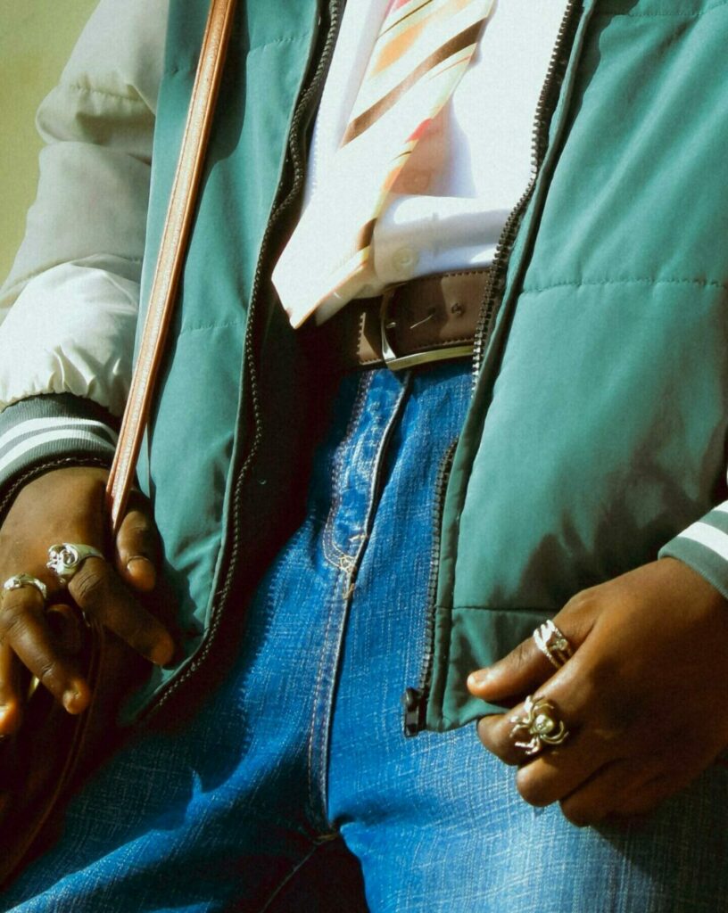 Stylish person wearing rings, tie, and a layered outfit, showcasing modern fashion.