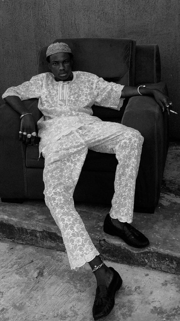 Stylish man in traditional attire seated casually in a monochrome setting.